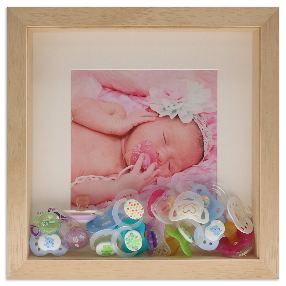 naturfarbener Objektrahmen gefüllt mit Babyfoto, Schnullern und weißem Passepartout