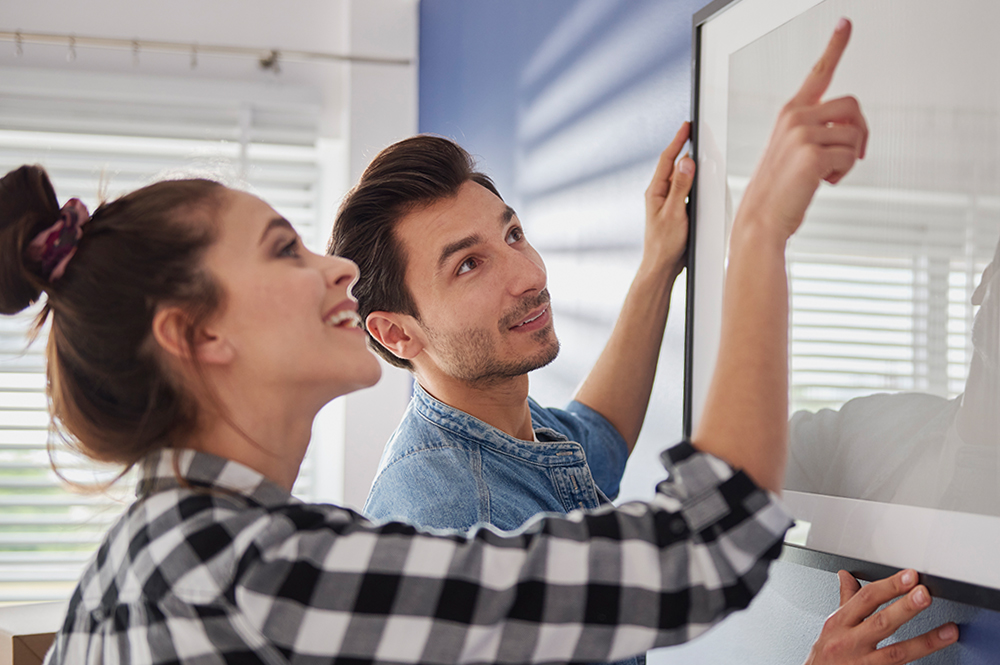 Poster mit Rahmen an einer Wand aufhängen Mann und Frau hängen Posterrahmen auf