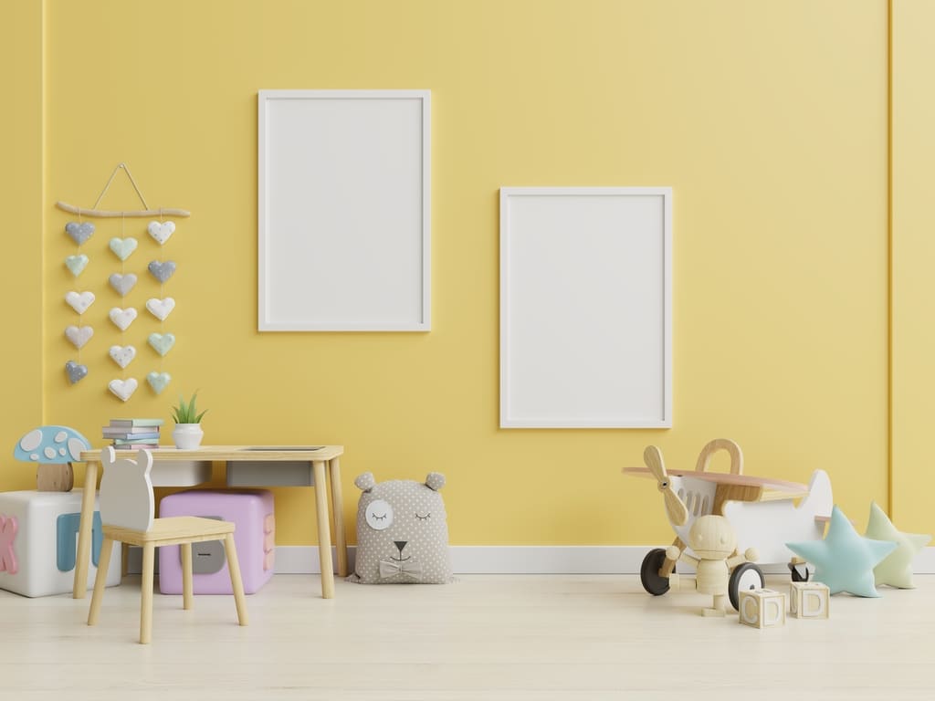 in Gelb gestrichenes Kinderzimmer mit Spielzeugen und weißen Bilderrahmen
